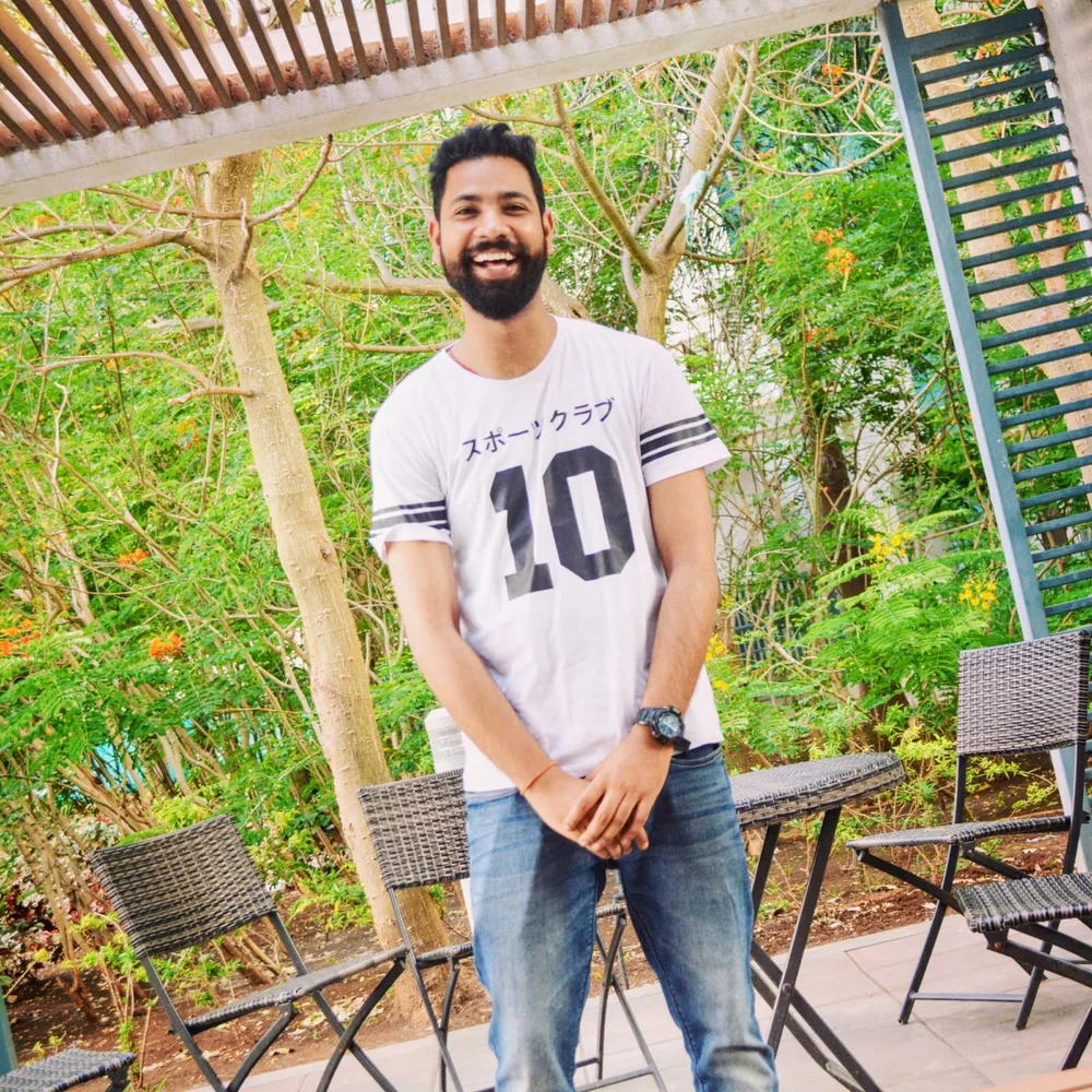 Rahul laughing outdoors beneath a wooden pergola